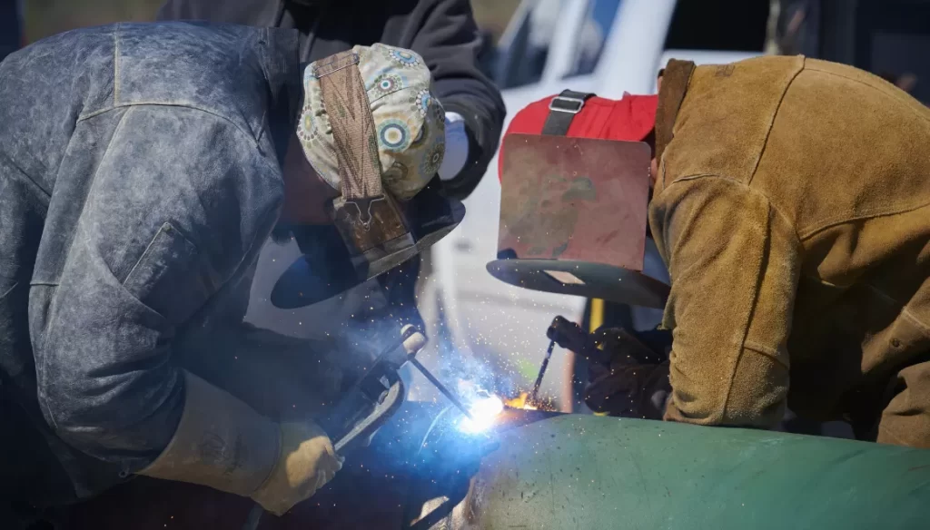 Two people with masks welding pipe